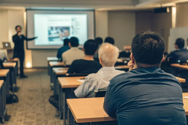 Arka tarafında oturan ve toplantı odası, olay ve seminer kavramı düşük ışıkta sahnede speackers dinleme kitlelere