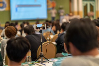 Closeup akıllı cep telefonu alarak ayakta ve bilgi sahne alanı'nda vererek konferans salonu veya Seminer Toplantı, iş ve eğitim kavramı casual elbise ile Asya konuşmacı dinleyiciye ile akış Live