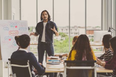 Asya Yaratıcı Yöneticisi, Asyalı İş Adamları Grubu 'nun önünde modern iş yerinde ciddi bir eylem içinde olan günlük kıyafetle başarılı fikirleri sunuyor.