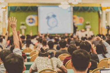 Konferans salonu veya Seminer Toplantı, iş ve eğitim kavramı sahne alanı'ndaki hoparlörden soruyu cevaplamak için el gösterilen seyirci arkadan görünüş