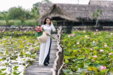 Büyük lotus gölü, Vietnam, aisan veya güneydoğu Asya seyahat konsepti ahşap köprü üzerinde yürüyen pembe lotus tutan geleneksel Vietnam şapkalı güzel Vietnamlı kadın portresi