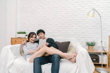 Mutlu Asya oturan ve dijital teknoloji tablet modern ev, oturma odası kanepe üzerinde selfie için çift başarılı ve yaşam tarzı kavramı kullanarak sevgilisi