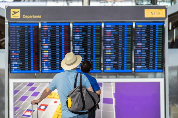 現代空港のフライト情報画面 旅行および輸送技術概念でチェックインのフライト ボードに立っている荷物を持つ旅行者の裏側します — ストック写真