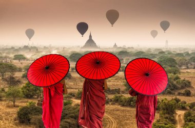 Arka yüzünde üç Budist acemi yürüme Bagan eski tapınaklarda üzerinde sıcak hava ile gökyüzü üzerinde gündoğumu zaman, Myanmar