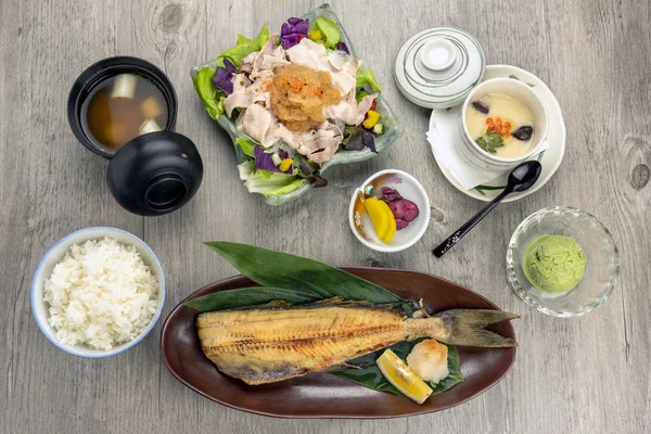 Top view of japanese foods set, fried fish serve with stream rice and pork yum salad with egg stream, soup and ice scream over the wooden table, luxury japanese food concept