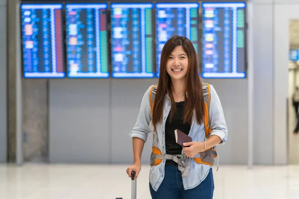 亚洲旅客带着护照携带行李走在航班板上 在现代机场的航班信息屏幕上办理登机手续 旅行和运输与技术概念 — 图库照片