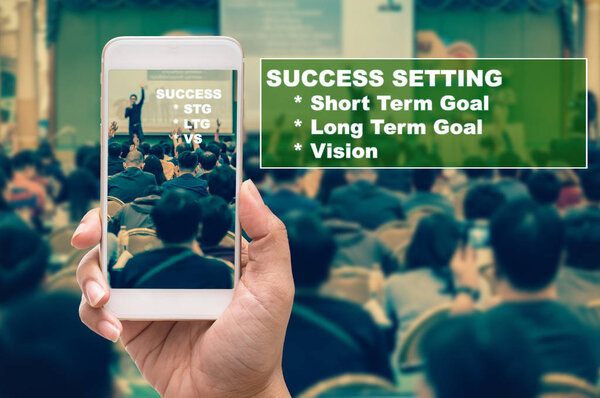 Hand holding smart mobile phone showing the Augmented Reality or AR technology over the Abstract blurred photo of conference hall or seminar room with speaker giving speech of success background