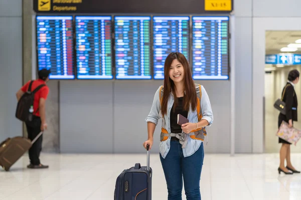 亚洲旅客带着护照携带行李走在航班板上 在现代机场的航班信息屏幕上办理登机手续 旅行和运输与技术概念 — 图库照片