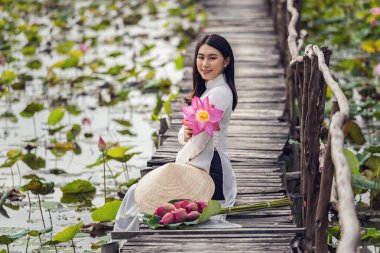 Büyük lotus gölü, Vietnam, aisan veya güneydoğu Asya seyahat konsepti ahşap köprü üzerinde oturan pembe lotus tutan geleneksel Vietnam şapkalı güzel Vietnamlı kadın portresi