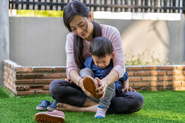 Asian single mom ware shoes to son on the front lawn of modern house for Self learning or home school, Family and single mom concept, selective focus