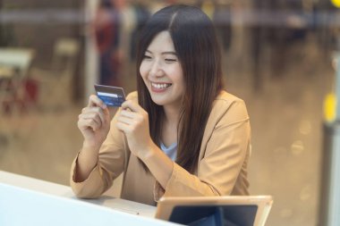 Asyalı bir kadın mağazadan alışveriş yapmak için cep telefonu kullanıyor. Giyim mağazası geçmişi, teknoloji para cüzdanı ve online ödeme konsepti, kredi kartı modeli.