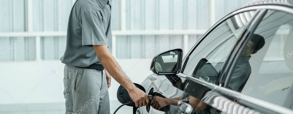 Senior asian Technician is charging the electric car or EV in service center for maintainance, Eco-friendly alternative energy concept