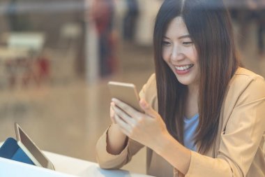 Asyalı bir kadın mağazadan alışveriş yapmak için cep telefonu kullanıyor. Giyim mağazası geçmişi, teknoloji para cüzdanı ve online ödeme konsepti, kredi kartı modeli.