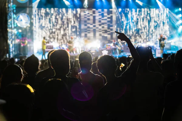 Concert crowd in silhouettes of Music fanclub with show hand action which follow up the songer at the front of stage with follow light, musical and concert concept