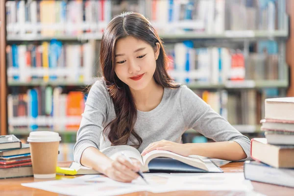 カジュアルなスーツを着たアジアの若い学生は 大学の図書館で読書や宿題をしたり 本棚の背景の上に木製のテーブルの上に様々な本や静止したコラージュで宿題をしています 学校に戻る — ストック写真