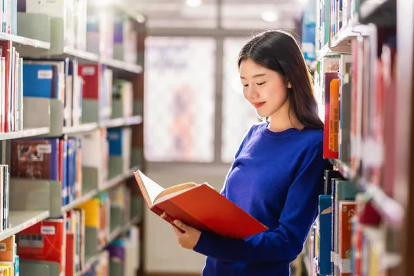 亚洲青年学生身着休闲服 在大学图书馆的书架上看书 或以各种书本背景 回到学校概念 — 图库照片