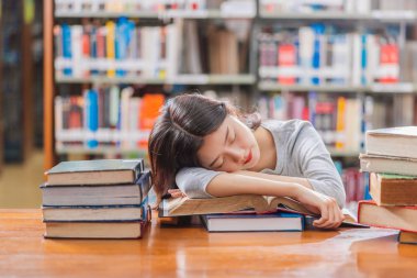 Rahat takım elbiseli Asyalı genç Öğrenci okuma ve kitap raf üzerinde üniversite veya kolaj çeşitli kitap ile ahşap masada uyku, Geri okul kavramı