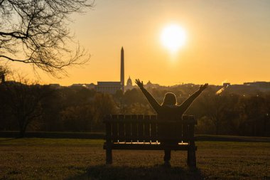 Asyalı bir kadının arkası, Washington DC 'nin başarısı için el kaldırıyor. Böylece Birleşik Devletler Kongre Binası, Washington Anıtı ve Lincoln Anıtı' nı gün doğumunda görebiliyoruz.,
