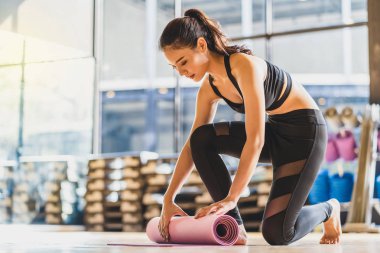 Asyalı genç kadın yoga sporundan önce ve sonra yoga minderini yuvarlıyor ve açıyor, sağlıklı ya da meditasyon egzersizlerine hazırlanıyor, spor sutyen ve pantolon giyiyor, spor ve sağlık konsepti takıyor.