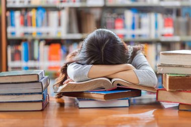 Rahat takım elbiseli Asyalı genç Öğrenci okuma ve kitap raf üzerinde üniversite veya kolaj çeşitli kitap ile ahşap masada uyku, Geri okul kavramı