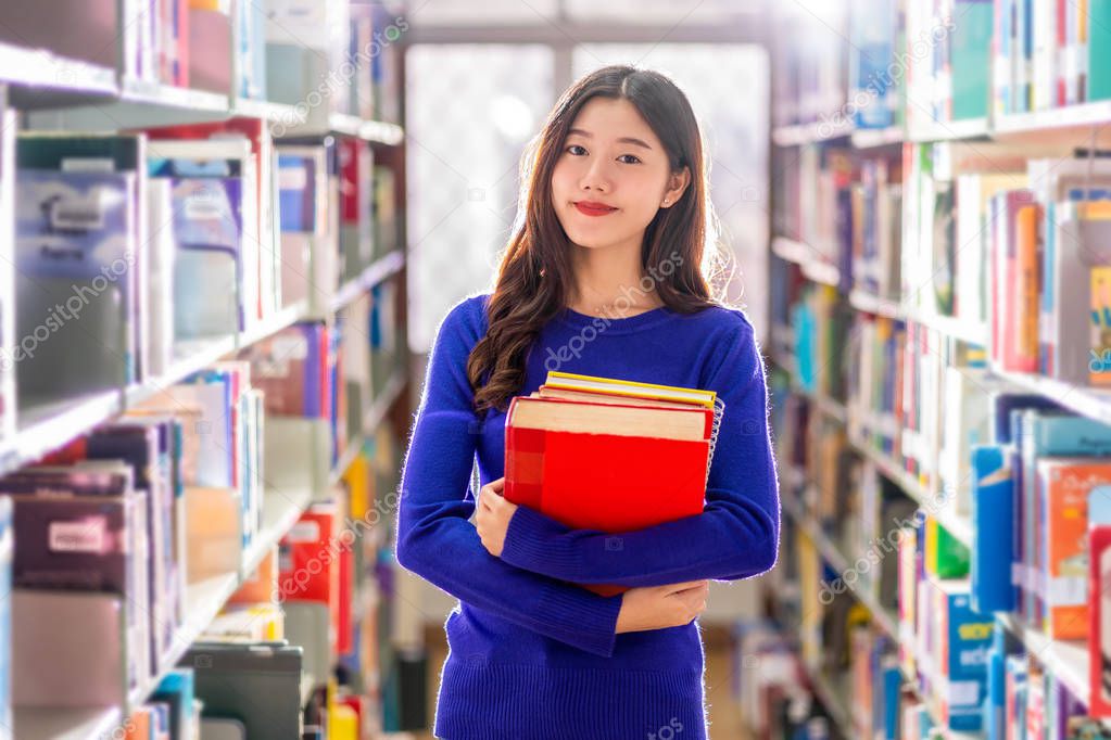 Asian young Student in casual suit holding after searching the book from book shelf in library of university or colleage with various book background, Back to school concept