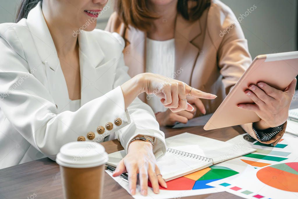 Closeup Two asian businesswomen working with the partner business by point finger to the technology tablet in modern meeting room, office or working space, coffee break, partner and colleague concept