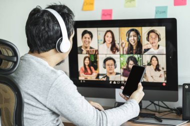 Covid-19 salgını, eğitim ve sosyal uzaklaşma, yeni normal bir kavram oluşturulduğunda, Asyalı bir adamın iş ve çevrimiçi toplantı için cep telefonunu kullanması ve iş arkadaşlarıyla video konferansı yoluyla ekip oluşturması