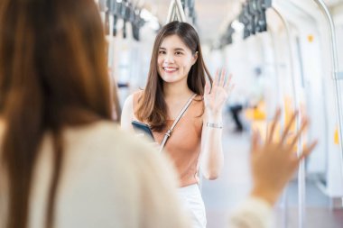 Genç Asyalı kadın yolcular cerrahi maske takıyor ve metroda arkadaşını selamlamak için el sallıyor. Covid19 salgınında büyük şehirde seyahat ederken, sosyal mesafeler ve yeni normal kavram.