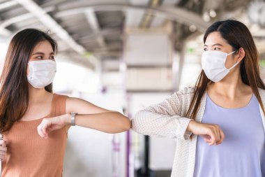 Cerrahi maske takan genç Asyalı kadın yolcular, Covid19 salgını, enfeksiyon ve salgın hastalıklar gibi yeni normal kavramlarla büyük bir şehirde seyahat ederken metro treninde arkadaşlarıyla çarpışıyorlar.