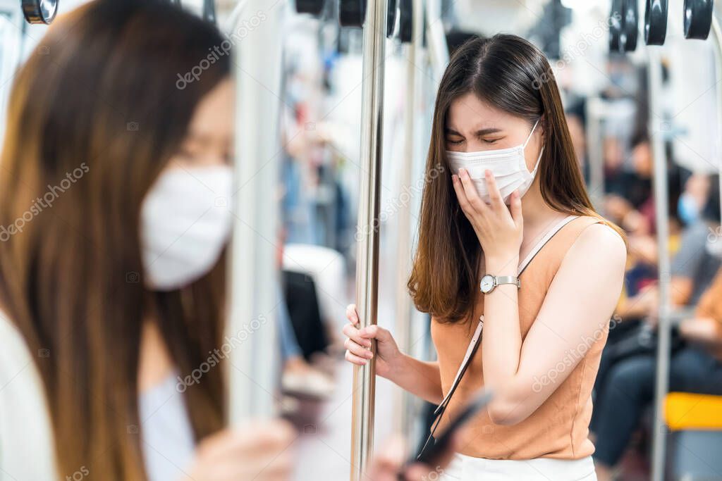 Young Asian women passengers wearing surgical mask and sneezing in subway train when traveling in big city at Covid19 outbreak, Infection and Pandemic, social distancing and new normal concept 