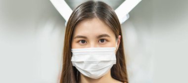 Genç Asyalı kadın yolcu cerrahi maske takıyor ve Covid19 salgını, salgın ve salgın hastalıklar, sosyal mesafeler ve yeni normal kavramlarla büyük bir şehirde seyahat ederken metro treninde kameraya bakıyor.