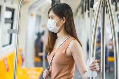 Genç Asyalı kadın yolcu, cerrahi maske takıyor ve metroda ıslak mendille ıslak mendil kullanıyor. Covid19 salgını, enfeksiyon ve salgın hastalıklar için büyük bir şehirde seyahat ederken.