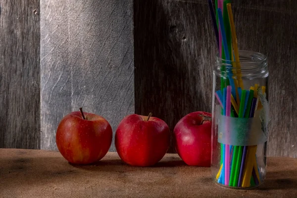 100 Isoクローズアップスタジオで撮影木製の背景にガラス瓶の中の3つの天然赤リンゴとプラスチックストローの写真 — ストック写真