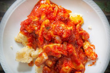 Polenta üzerine karışık domates soslu pişirilmiş tavuğun yakın plan fotoğrafı.