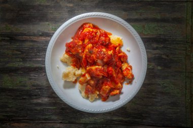  Ahşap masadaki Polenta üzerine karışık domates soslu kızarmış tavuk fotoğrafı.