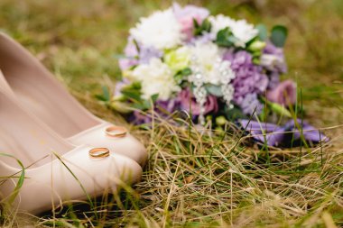 Bej düğün ayakkabıları, nişan yüzükleri, papyon ve çim buket çifti.