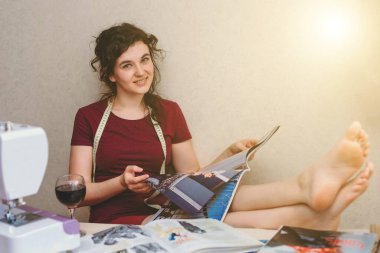 Mutlu ve çekici genç bayan terzi stüdyoda dikiş makinesine oturup dikiş dikiyor.