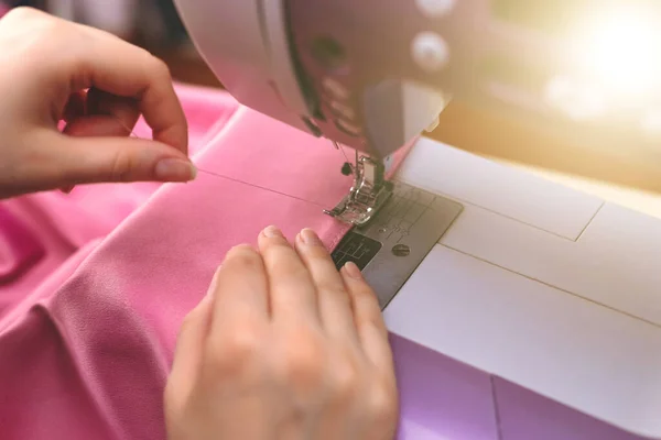 Happy attractive young woman seamstress sitting and sews on sewing machine in studio