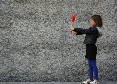 Küçük kız kırmızı rüzgar fırıldağıyla granit duvarda yürüyor.