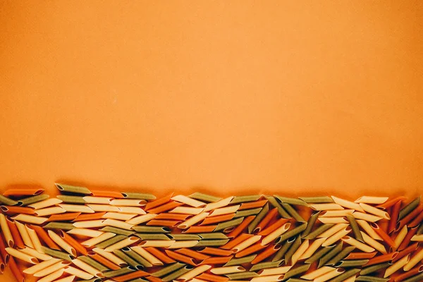 Ramka z kolorowego makaronu zielonego, żółtego i czerwonego penne naturalnie barwionego pomidorem i szpinakiem. — Zdjęcie stockowe