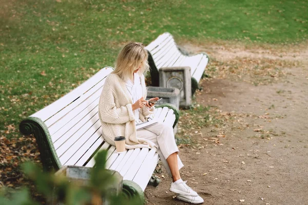 Genç iş kadını parkta bir bankta oturuyor ve telefonla konuşuyor.. — Stok fotoğraf