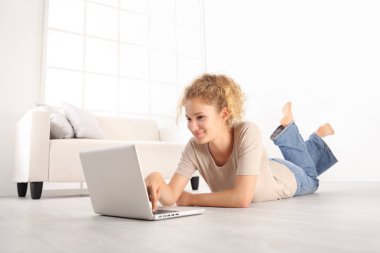 modern beyaz ev salon ahşap yerde yatarken, bir dizüstü bilgisayar kullanarak gülümseyen güzel genç kadın 