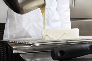 bir paslanmaz çelik endüstriyel mutfak iş üstünde çalışan bir kek, beyaz buzlanma, dökme kapak eller pasta şefi hazırlar