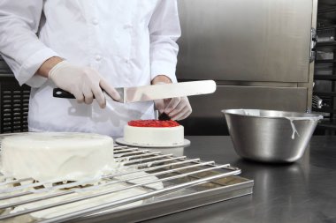 Eller pasta şefi bir pasta, krema ile kapak hazırlar ve çilek, paslanmaz çelik endüstriyel mutfak iş üst üzerinde çalışır ile süsleyin