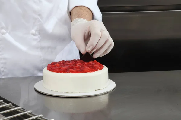 手パティシエ ケーキ アイシングでカバーを準備し ステンレス鋼産業の台所仕事上の作品 苺を飾る — ストック写真