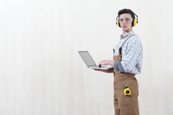 De mens van de timmerman met computer die op houten achtergrond met c wordt geïsoleerd — Stockfoto