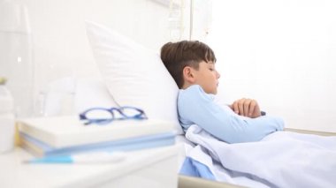 Hastanedeki çocuk uykuya dalıyor. Başını yastığa koymadan önce esniyor. Yatakta tek başına yatıyor.