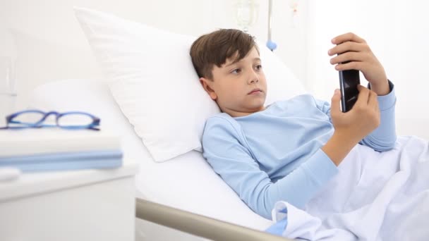 带着手机在医院里独自躺在床上笑着的孩子 — 图库视频影像