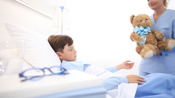 Uśmiechnięta Pielęgniarka Zajmuje Się Dzieckiem Leżącym Szpitalnym Łóżku Robiąc Niespodziankę — Wideo stockowe