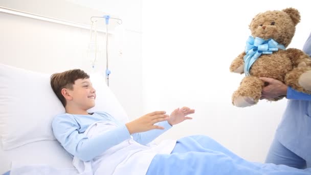 护士微笑着照顾躺在病床上的孩子 给了他一只泰迪熊 让他大吃一惊 — 图库视频影像